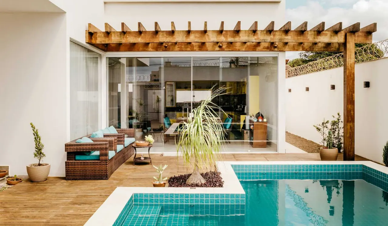 Área externa de uma casa com pergolado de madeira, deck e piscina